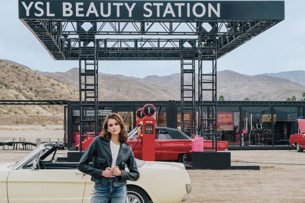 women in a leather jacket standing in front of cars at a YSL beauty gas station