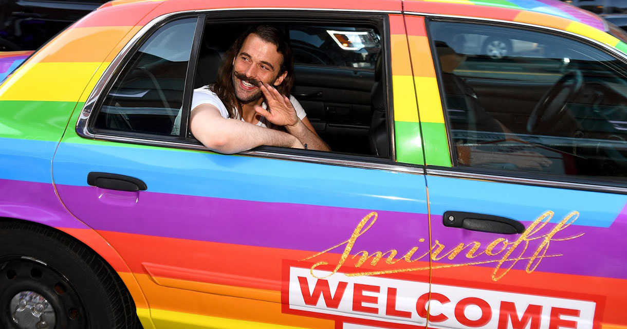 jonathan van ness in a smirnoff vodka rainbow taxi waving hello while smiling for the attention economy