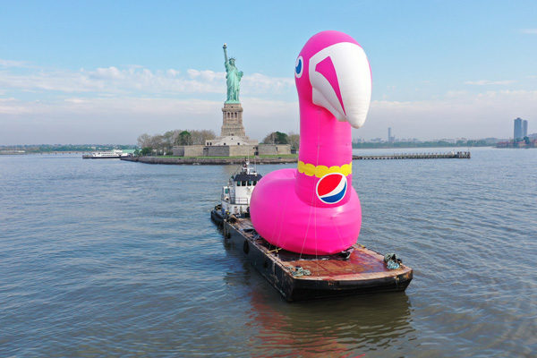giant pink flamingo inflatable floating at sea in front of the statue of liberty for brand activations