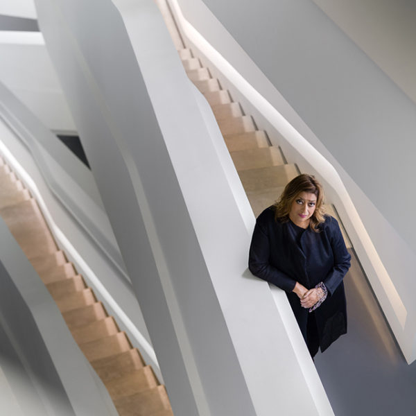 image of zaha hadid standing on white stairs looking up at the camera for women's history month