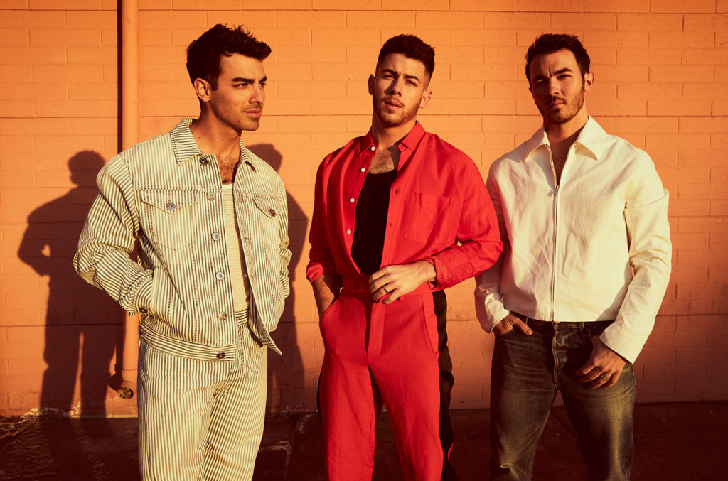 Jonas Brothers standing together against an orange background