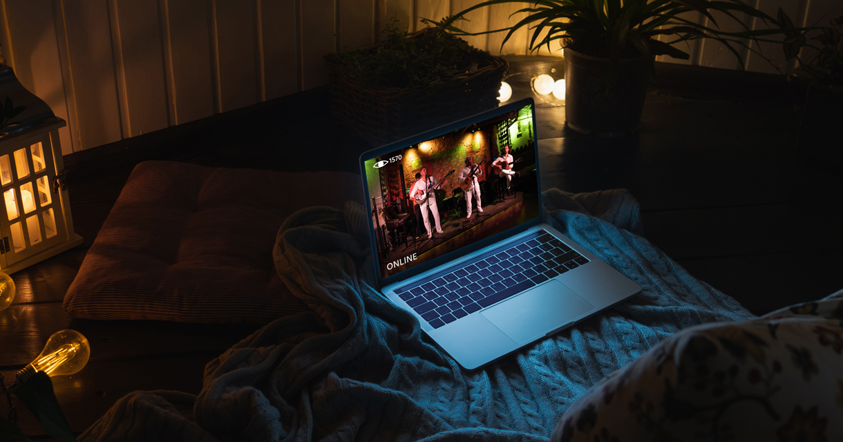 Laptop livestreaming a concert, sitting on top of a blanket in a cozy setting